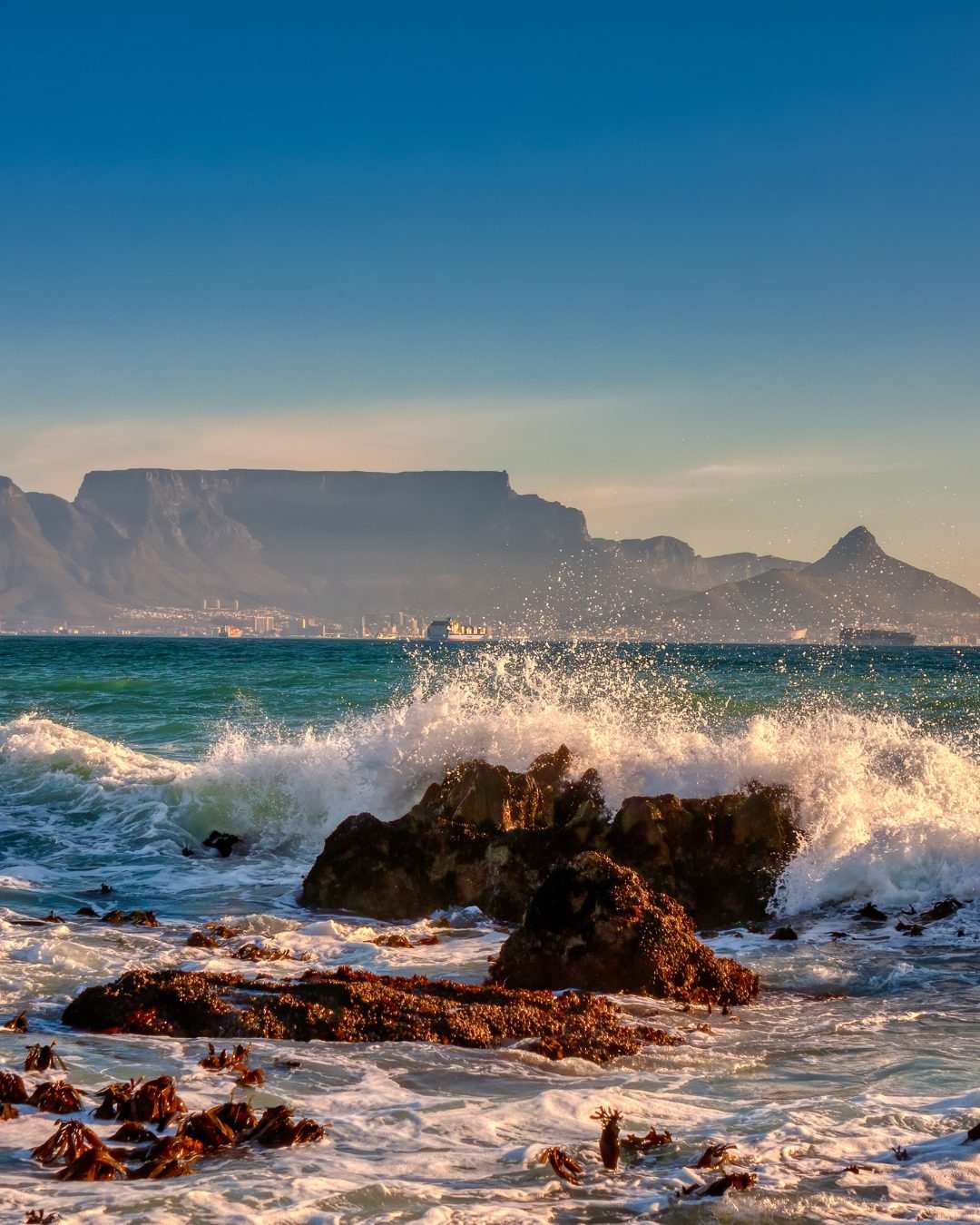 Ocean waves breaking on rocks with Table Mountain in the distance